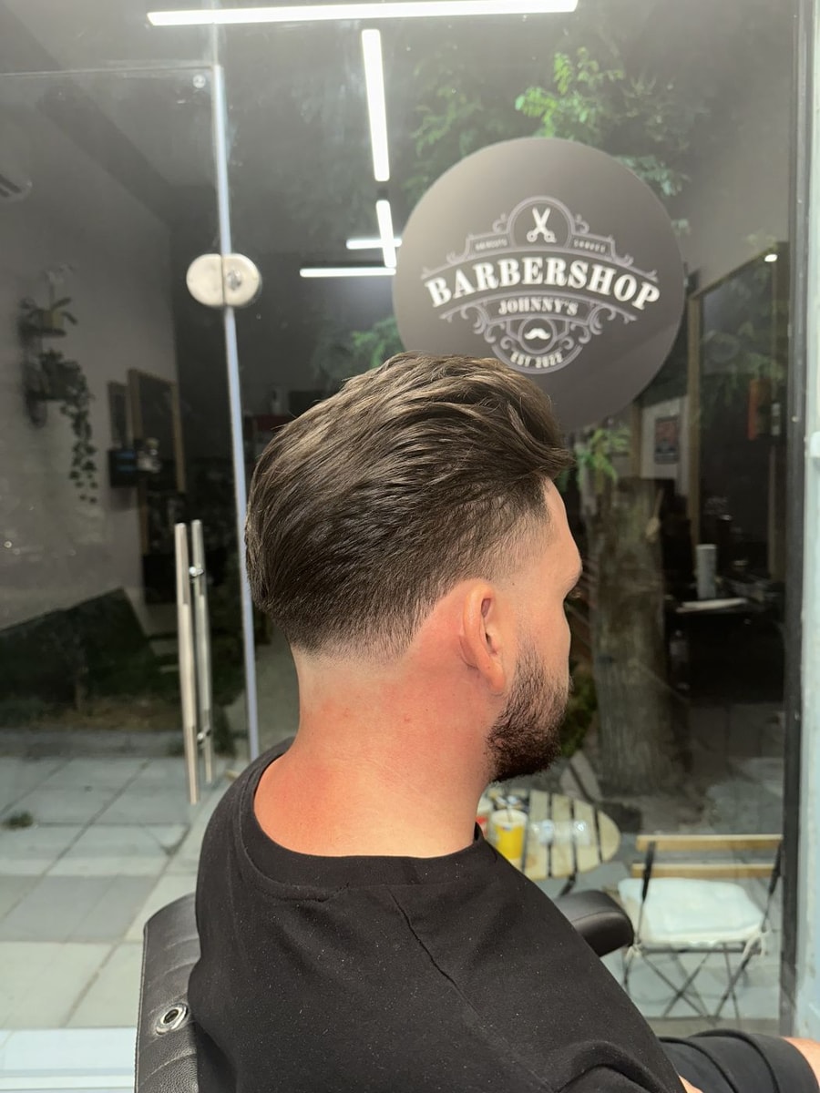 Ανδρικό κούρεμα taper από πίσω, δουλειά του JOHNNY'S BARBERSHOP, με το στρογγυλό σήμα του μαγαζιού στη τζαμαρία