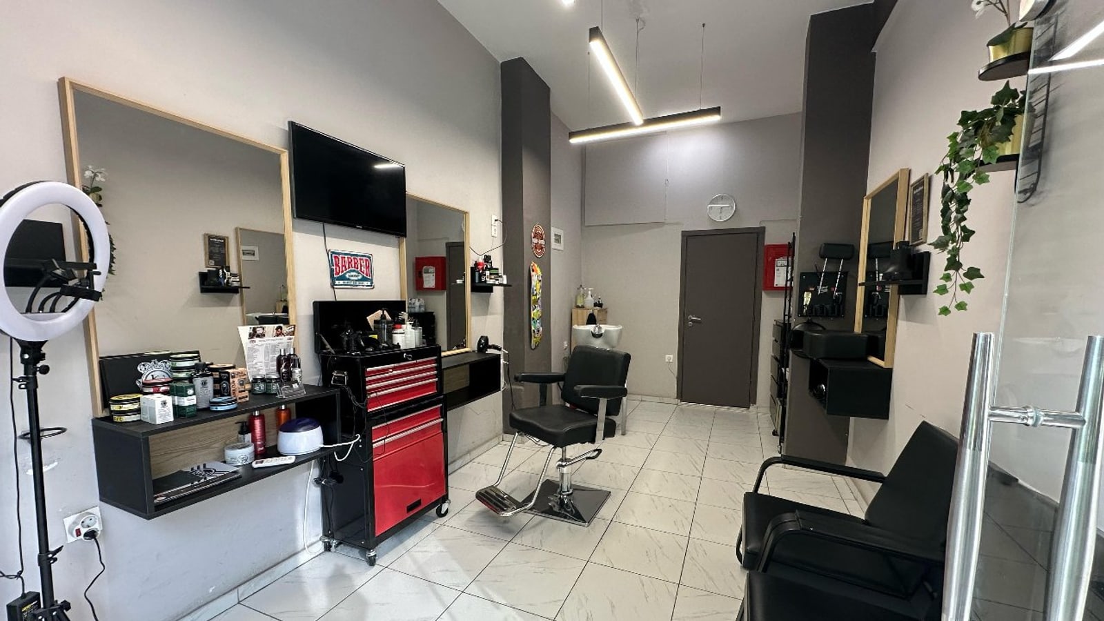 Ο χώρος του JOHNNY'S BARBERSHOP: λευκό μαρμάρινο δάπεδο, καθρέφτες με ξύλινη κορνίζα, κόκκινη εργαλειοθήκη και η μεταλλική πινακίδα BARBER